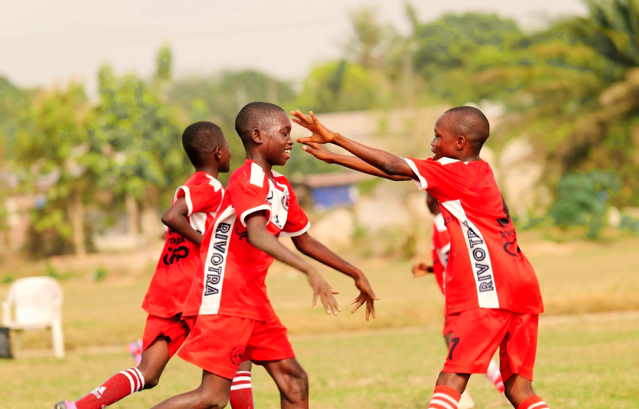 Photographie provisoire : trois jeunes joueurs du club se congratulent après un but, sur un terrain en herbe.