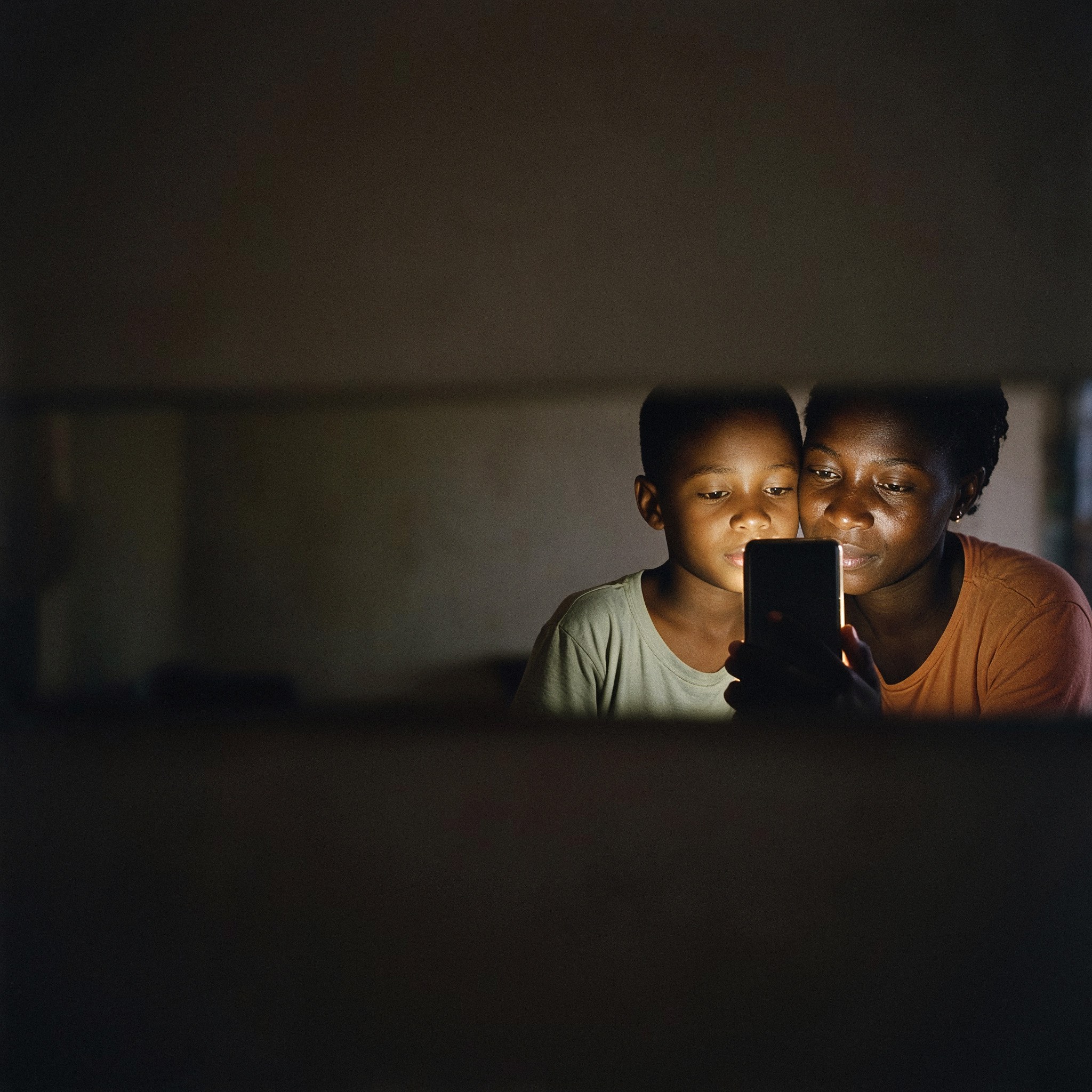 Une mère et son fils, le soir dans leur salon, regardent ensemble l'application sur un téléphone.